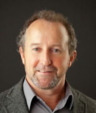 Portrait of a middle-aged man in a gray blazer and shirt against a dark background.