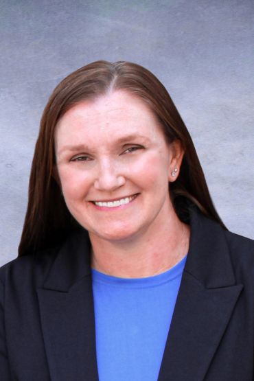 Woman smiling in professional attire against a neutral background.