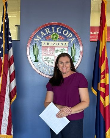 Woman standing in front of Maricopa County seal with flags.