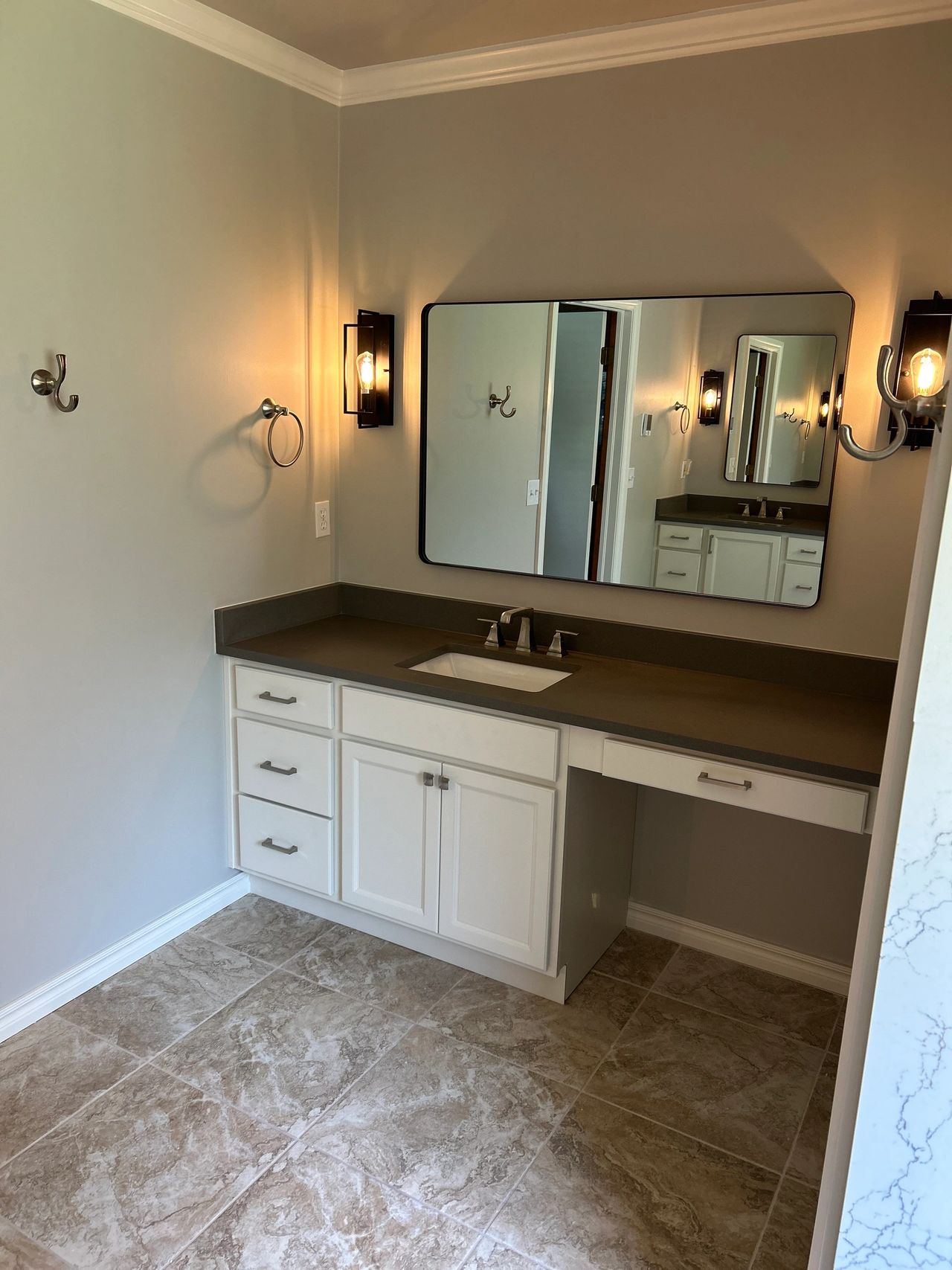 This is her side of the bathroom with the knee space to put on her make up and plenty of upgraded storage from her old vanity.  It has the white shaker style cabinets with the matte gray quartz countertops with an undermount rectangle sink.  It also features the framed mirror and sconce lighting.