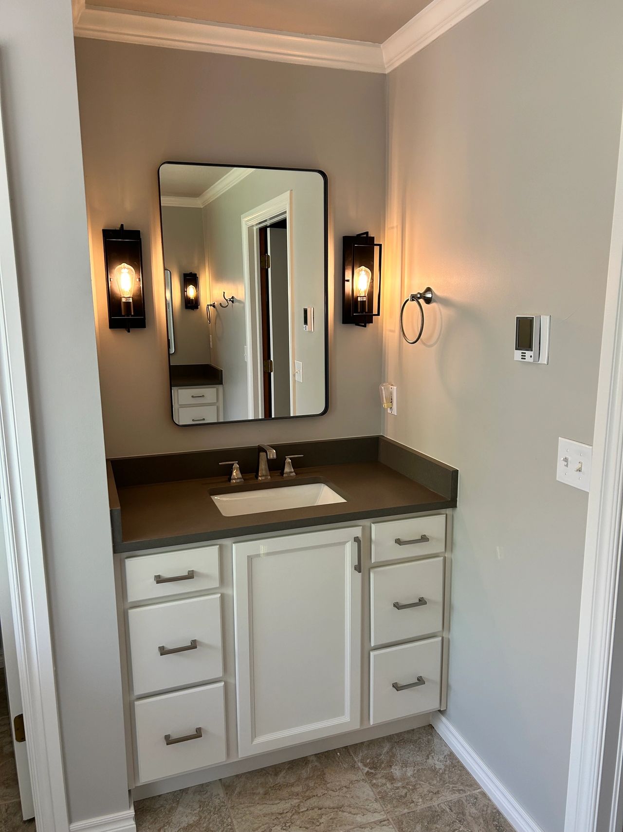 His vanity cabinet with the white shaker style cabinets and the matte gray quartz countertop.  His side features the taller framed mirror to fit his height as well as new sconce lighting.