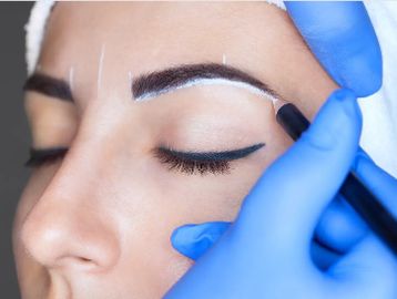 A person gets eyebrow shaping with white markings and black pencil.
