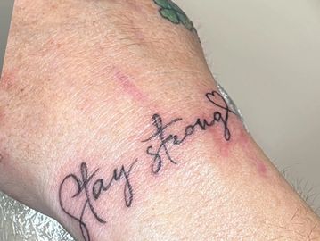 Tattoo on wrist reading 'Stay strong' with a small heart.