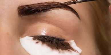 Applying dark eyebrow tint to enhance brow shape.