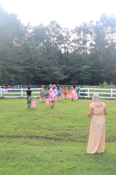 Group of women walking on grass carrying pink buckets.