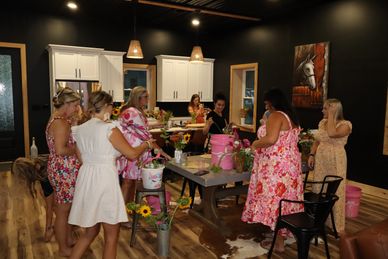 Group of women gathering indoors around a table with flowers.