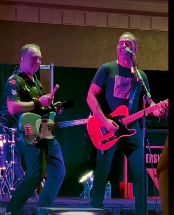 Two musicians passionately perform on stage with guitars under colorful lights.