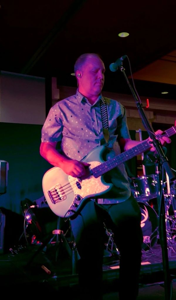 Man playing bass guitar on stage under purple lighting.