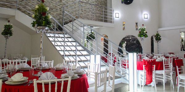 Elegant dining area with red-covered tables and floral centerpieces near a modern staircase.