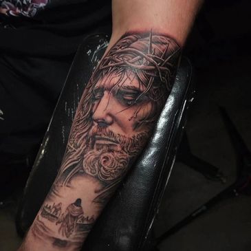 Realistic tattoo of Jesus Christ wearing a crown of thorns on forearm.