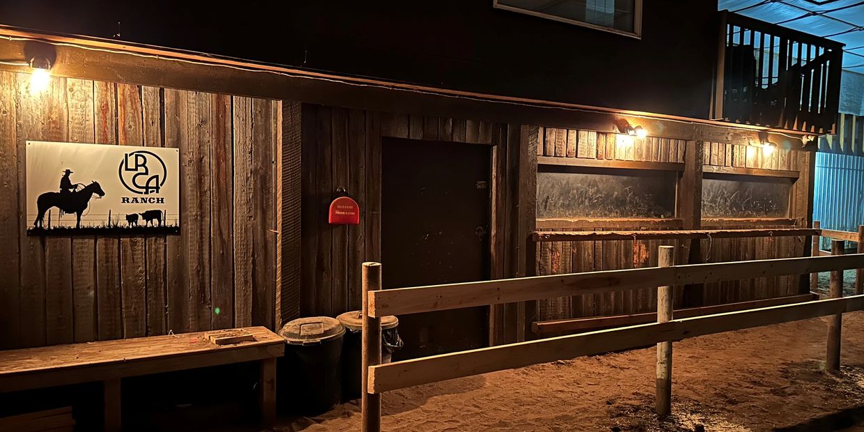 Rustic ranch building illuminated at night with wooden fences and a ranch sign.