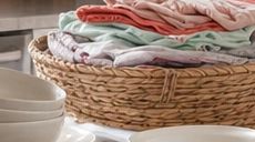 Folded clothes in a wicker basket with white bowls nearby.