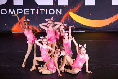 Seven young dancers in pink costumes hitting their final pose onstage at Ignite Dance Competition.