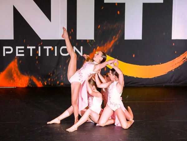 One dancer is being supported by the rest of the group onstage at Ignite Dance Competition.