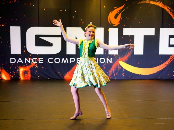 A musical theatre dancer in a green and yellow costume onstage at Ignite Dance Competition.