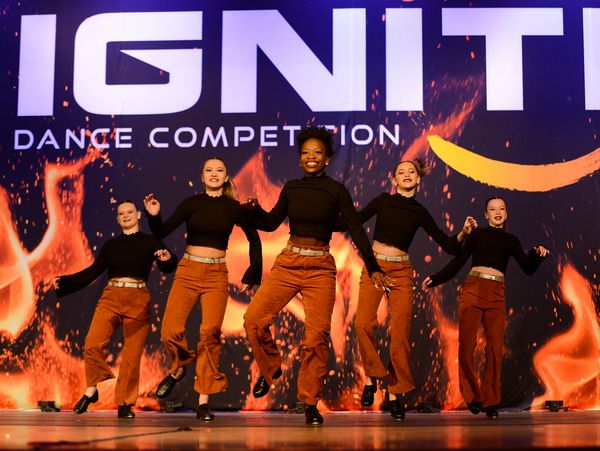 Five tap dancers onstage in orange pants and black turtlenecks