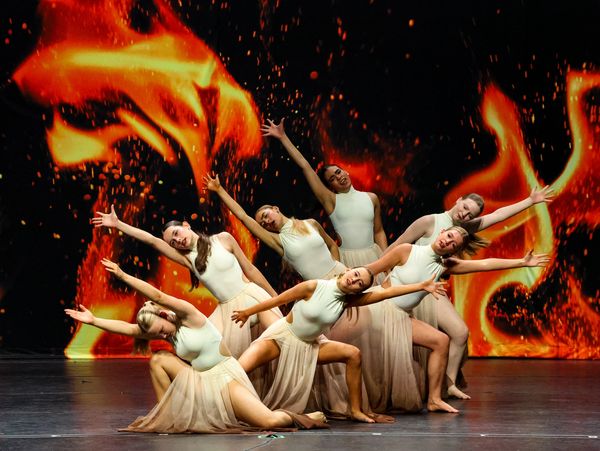 A group of contemporary dancers in cream dresses reaching out in a pose on the Ignite stage