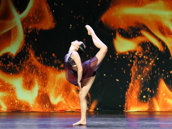 A dancer in a back attitude in a purple costume on the Ignite stage
