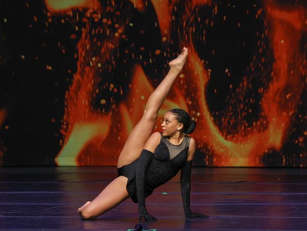 a dancer on the floor in a leg extension in a black costume on the ignite dance competition stage