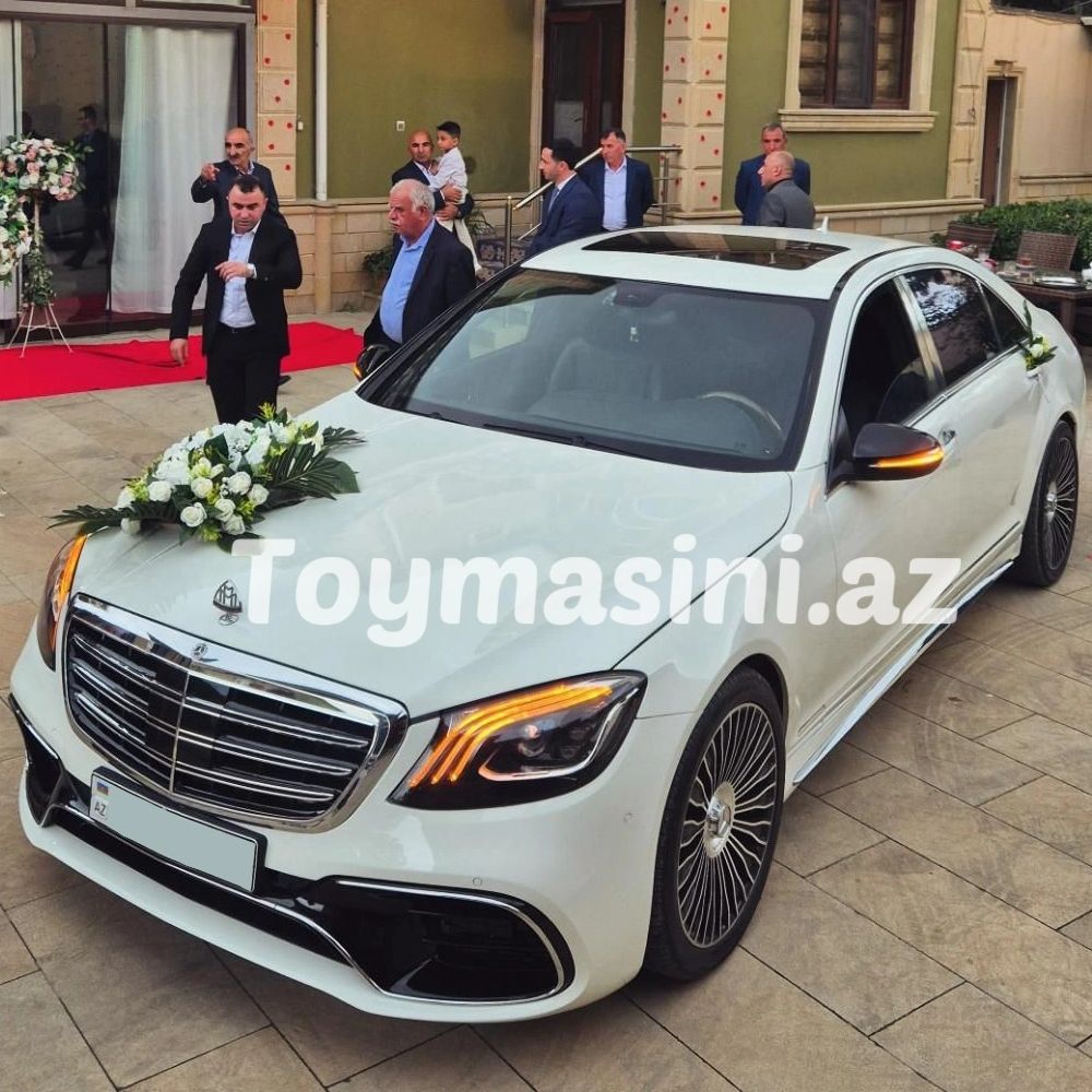 White luxury wedding car with floral decorations and people gathered around.