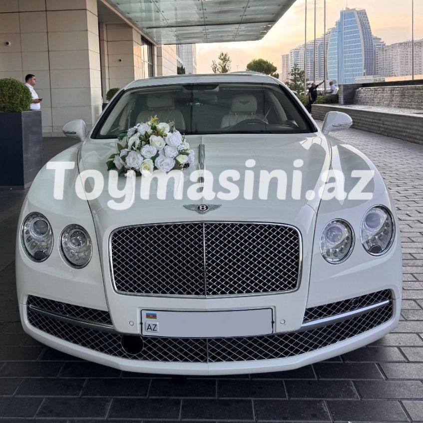 White Bentley with flower bouquet on hood, parked under glass canopy.