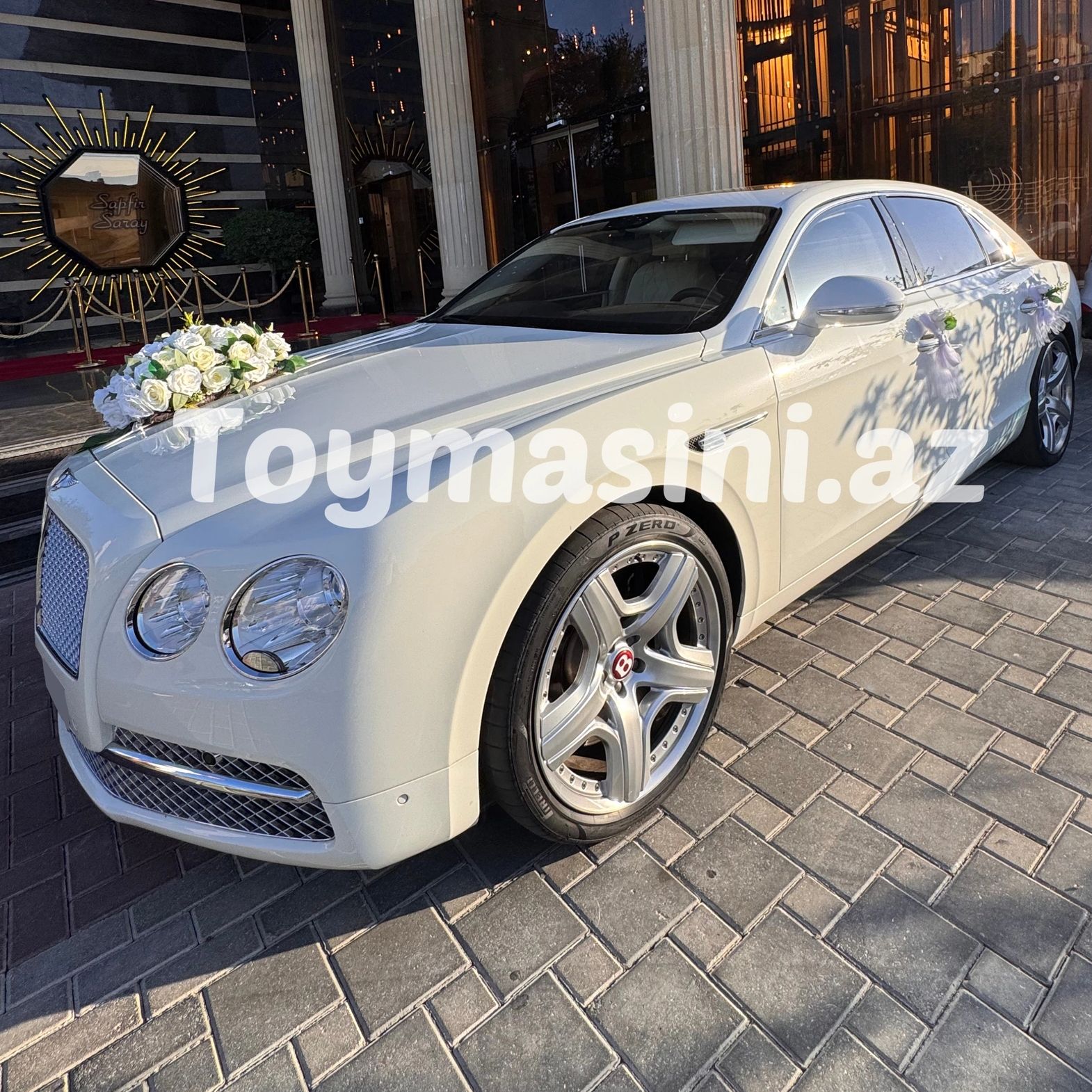 White luxury Bentley car decorated with white flowers, parked outside an elegant building.