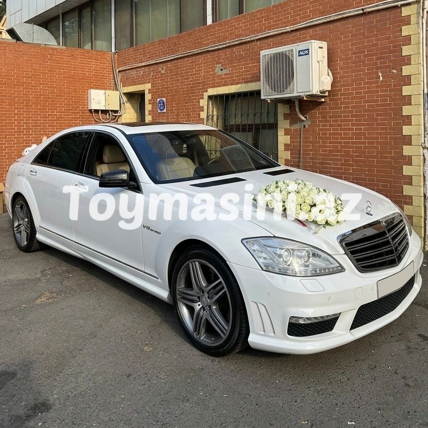 White Mercedes-Benz with floral decoration on the hood, parked by a brick wall.