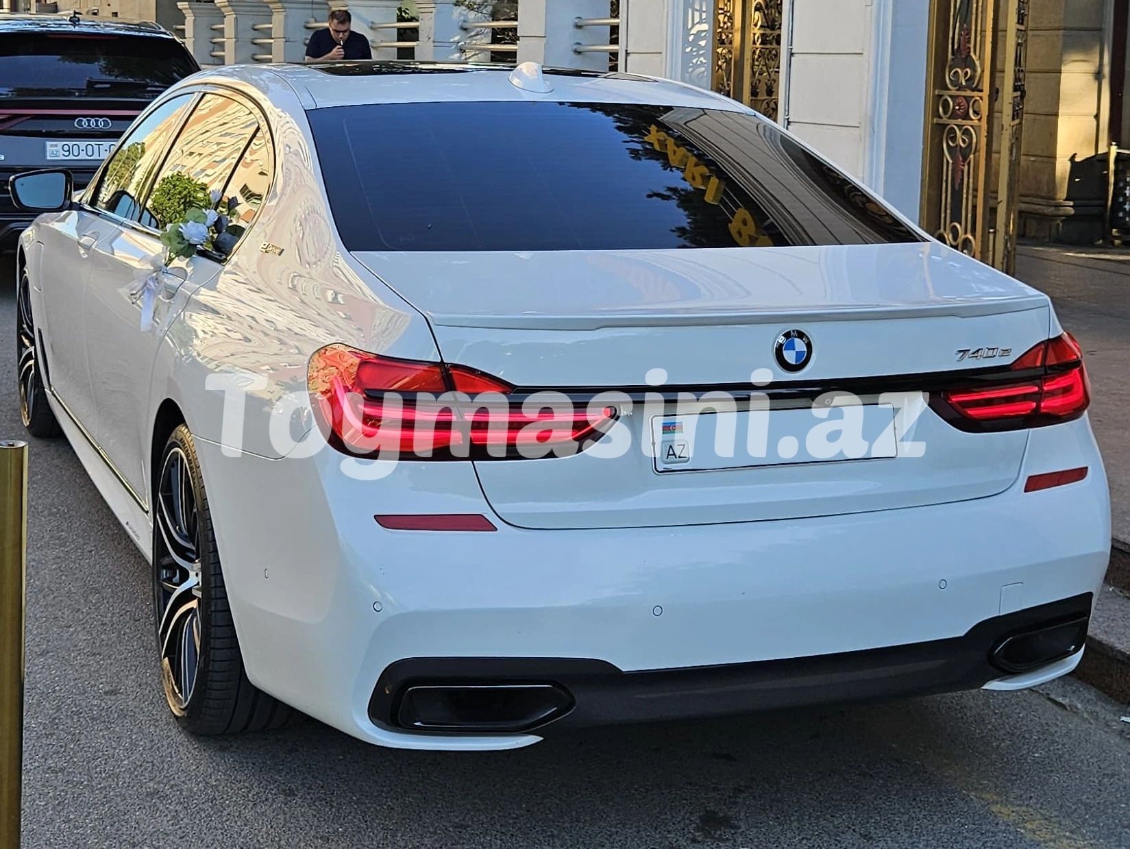 Arkadan beyaz BMW 740e araç ve yan aynada çiçek süslemeleri.