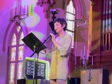 Woman singing on stage in a colorful lit church setting.