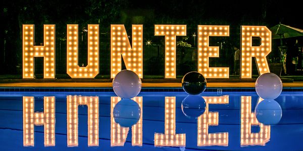Illuminated "HUNTER" sign reflected in a pool at night with balloons.