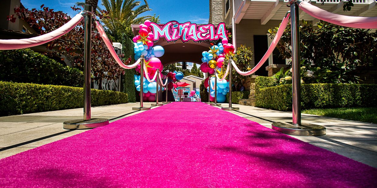 Bright pink carpet leads to a colorful party arch with balloons and the name "Mikaela".