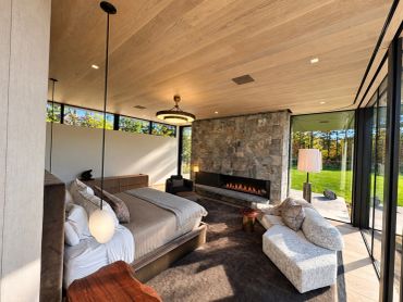 Modern bedroom with stone fireplace and large windows.