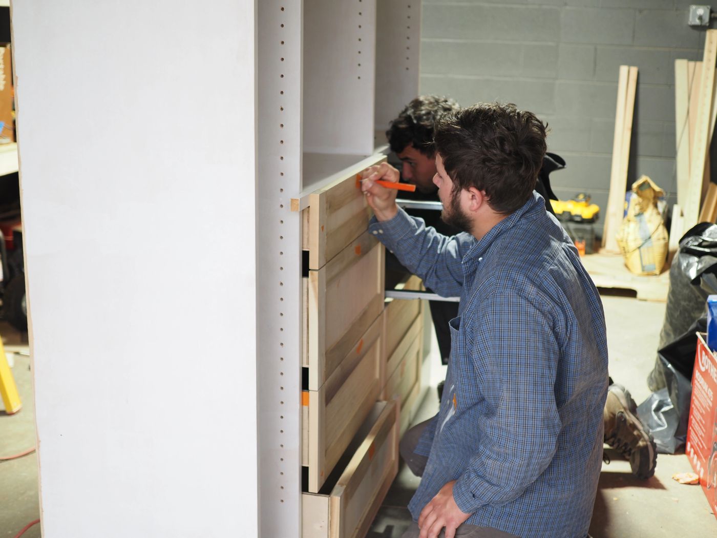 Two carpenters marking out a run of cabinet drawers in the shop