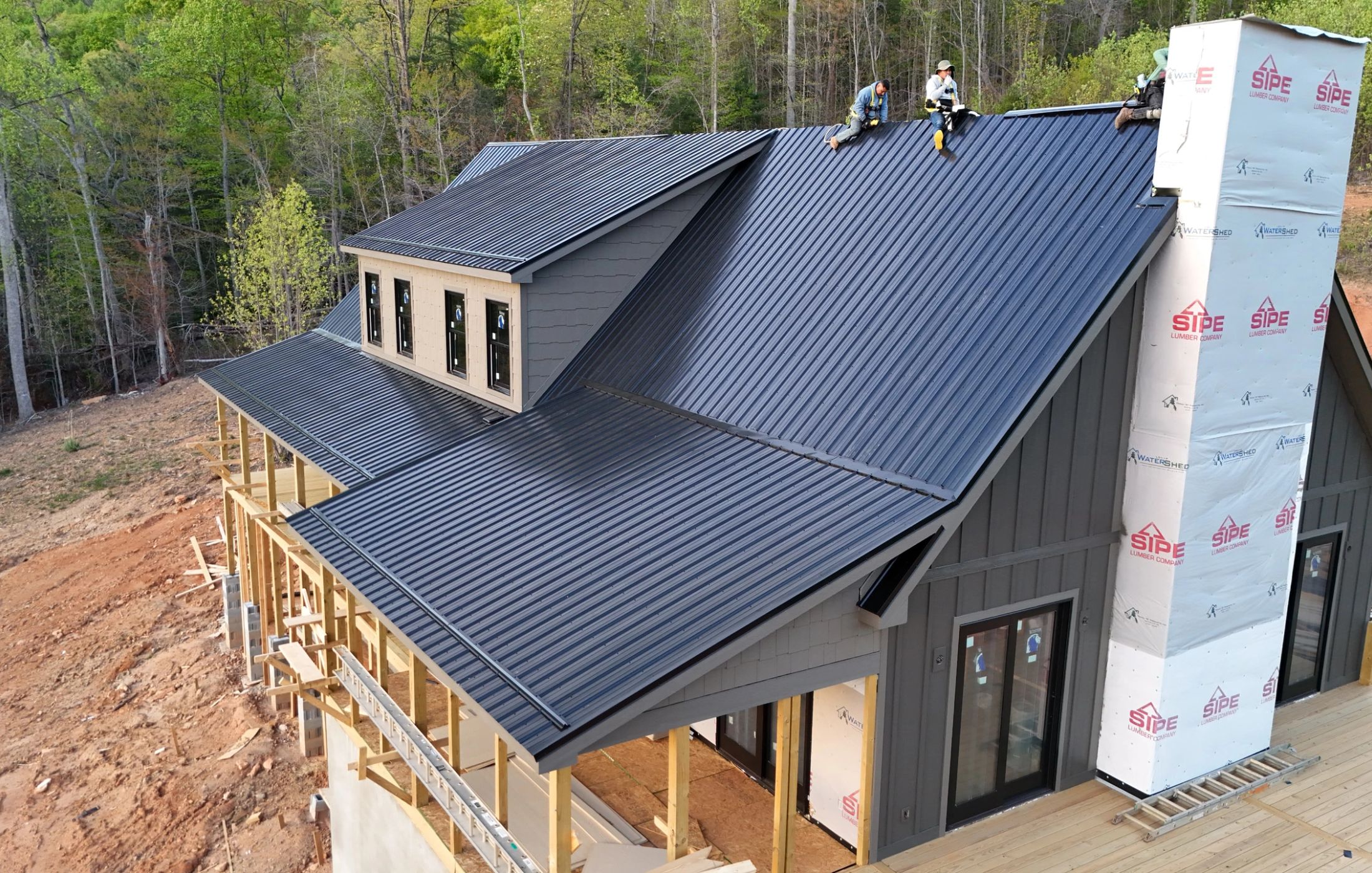 Aerial view of the standing seam roof nearing completion, crew working at the ridge