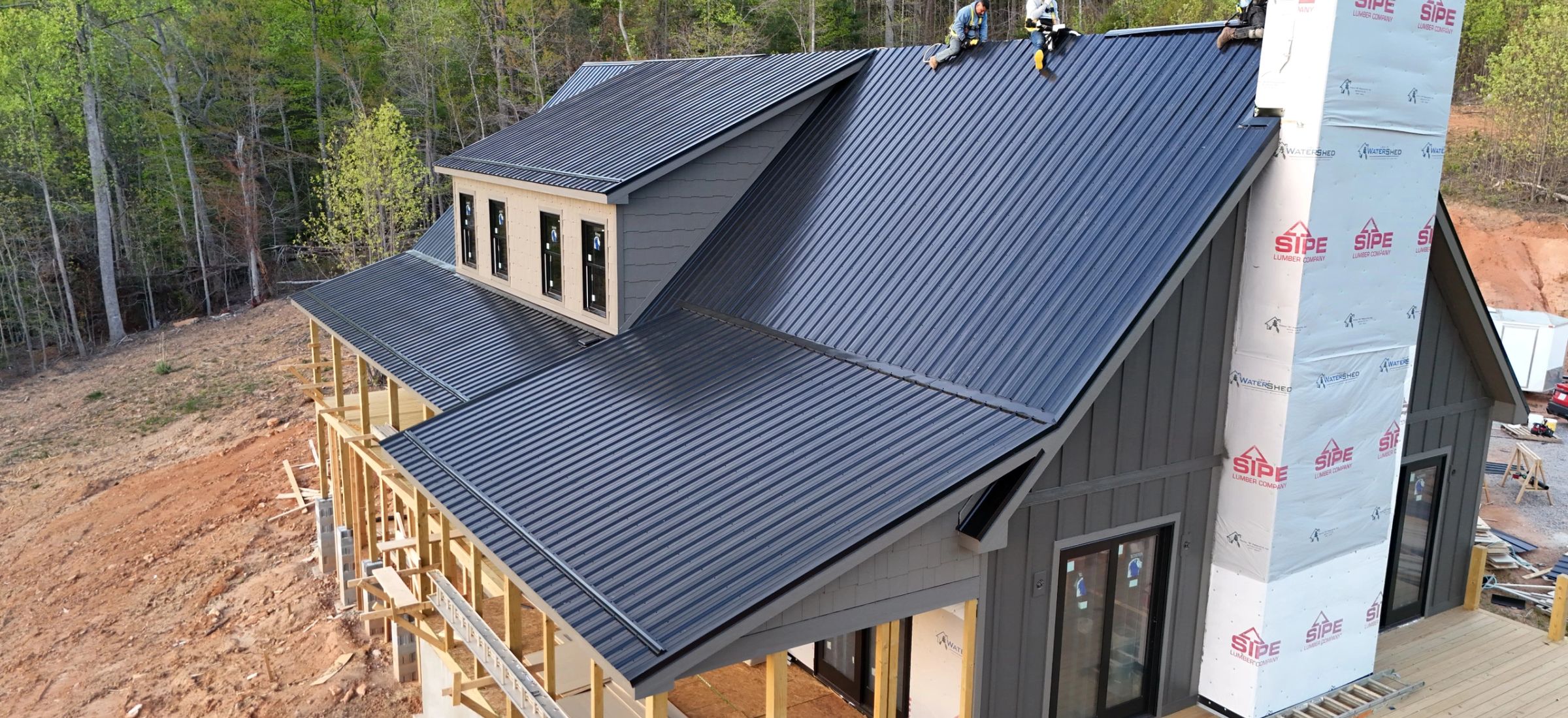 Aerial view of a standing seam metal roof being installed, crew working at the ridge
