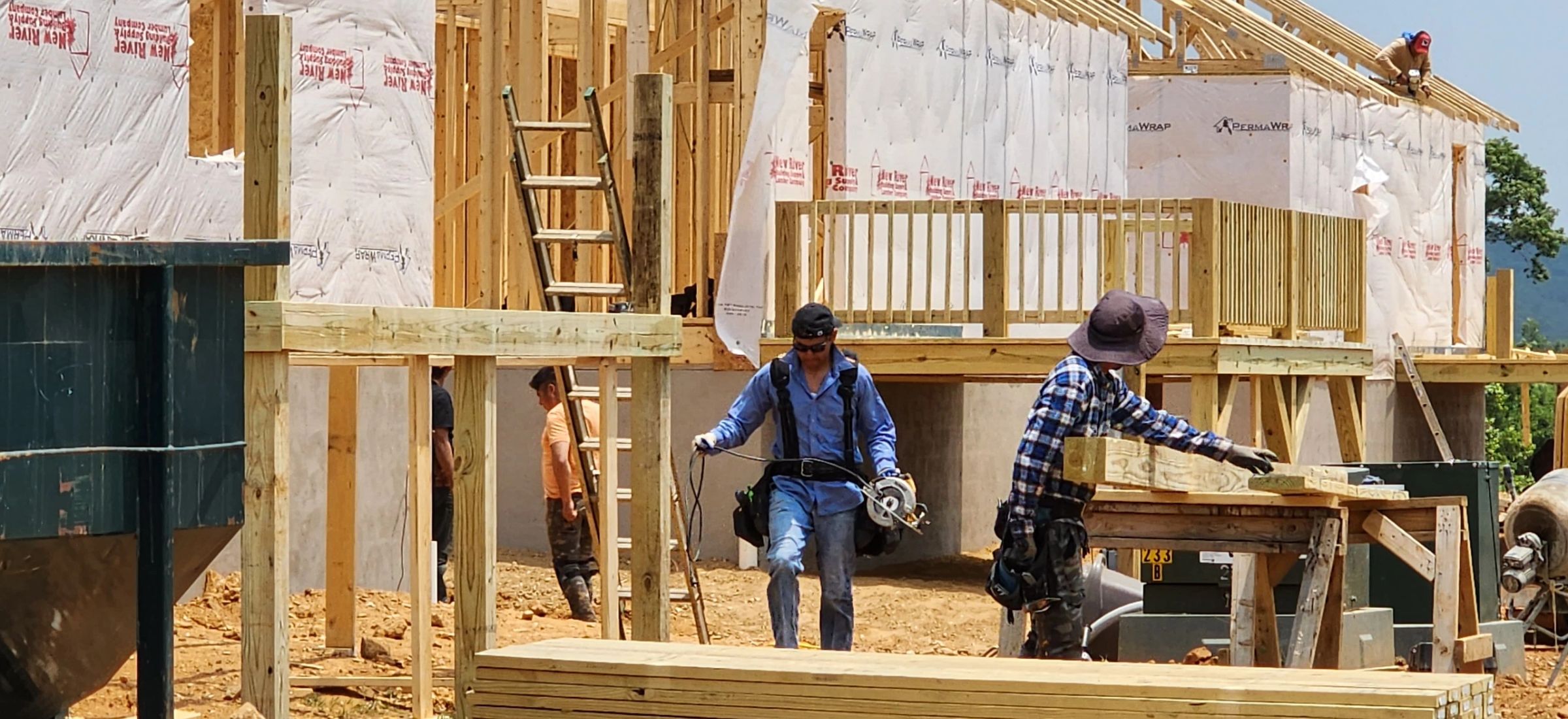 Crew framing walls and installing sheathing, mountains in the distance