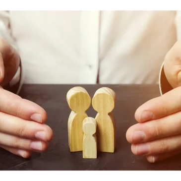 Hands protect a small wooden family figurine on a table.