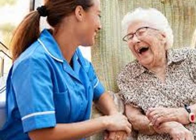 Smiling female caregiver sitting outside with a laughing elderly woman.