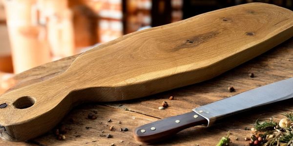 A wooden cutting board and a knife on a rustic wooden table.