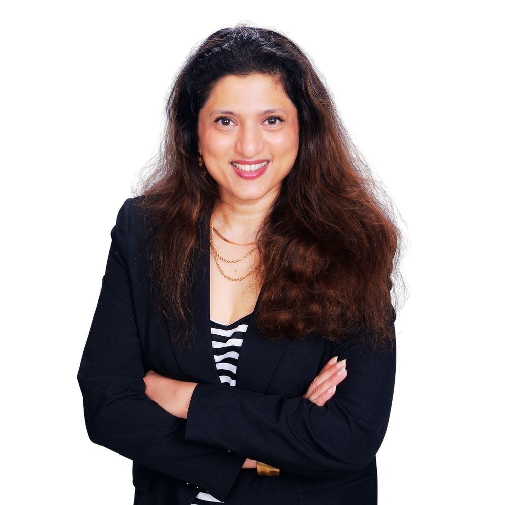 Confident woman with long hair, smiling, arms crossed, wearing a black blazer and striped top.
