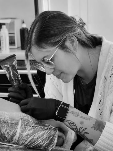 Tattoo artist focused on work, wearing gloves and glasses.