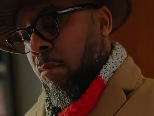 Man wearing glasses, a hat, and a colorful scarf.
