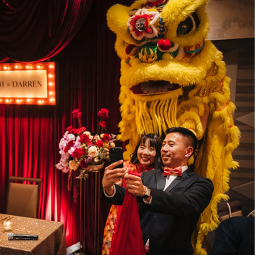Couple taking a selfie with a yellow lion dance costume at celebration.