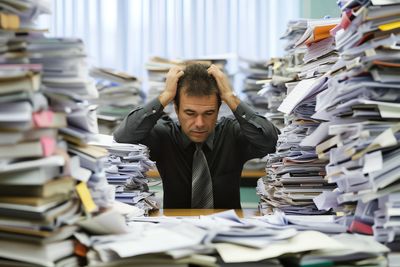 Stressed man surrounded by piles of paperwork.