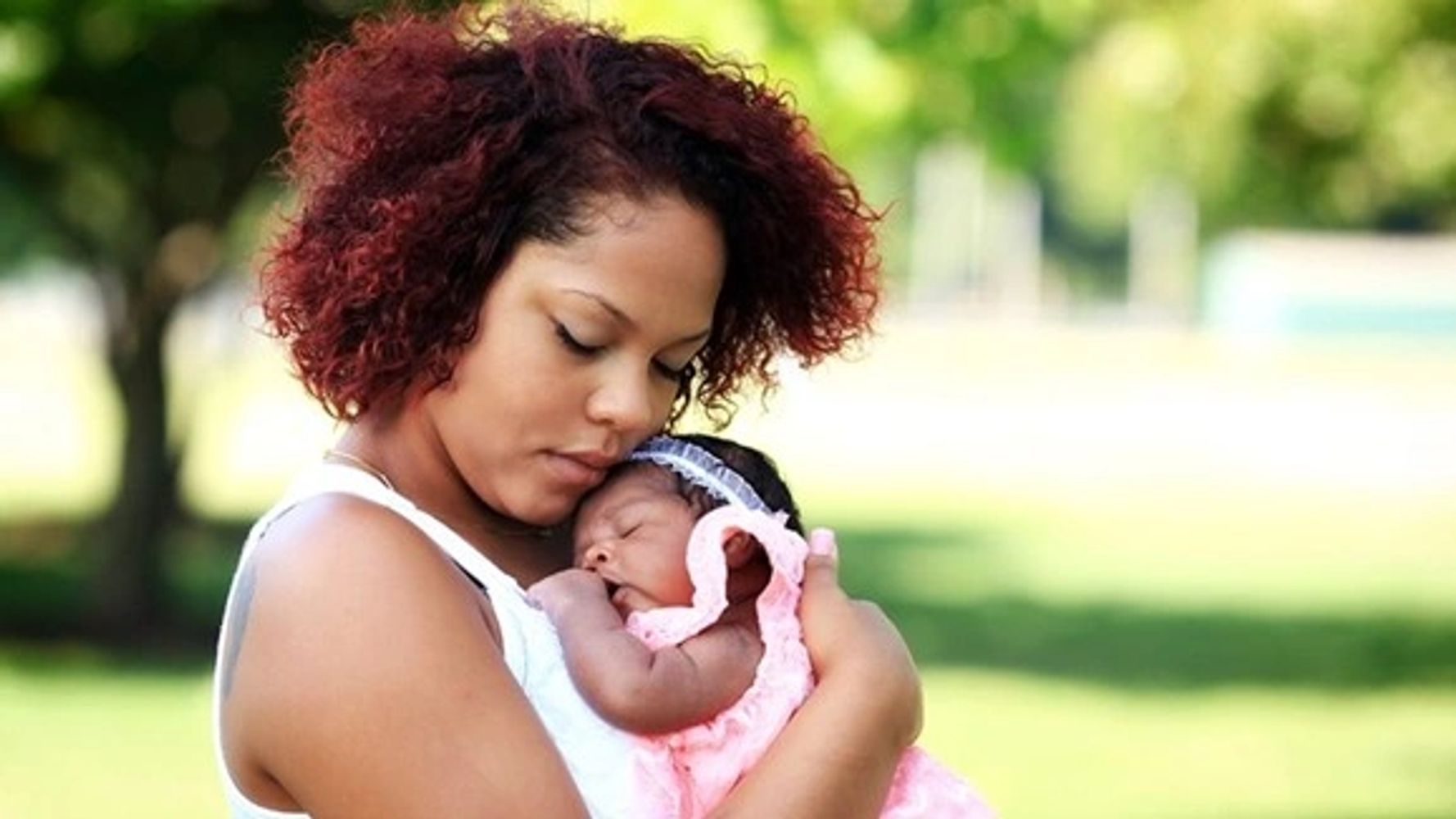Woman holding her infant baby with blurred outdoor background