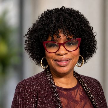 Smiling woman with curly hair and red glasses.