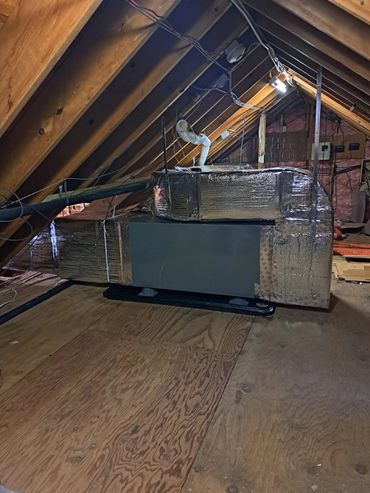 HVAC unit installed in a wooden attic space with exposed beams.