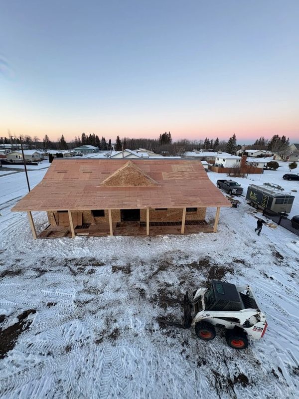 A wooden house under construction in a snowy area with a small bulldozer nearby.