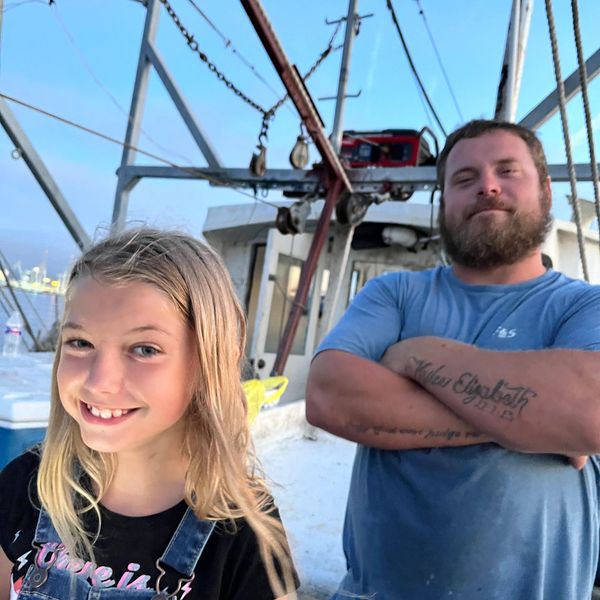 A smiling girl and a bearded man with tattoos on a boat at dusk.