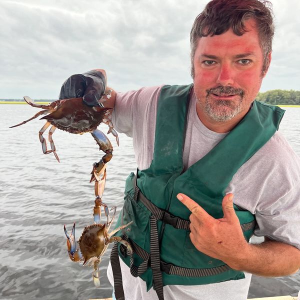 Man on a boat holding two blue crabs proudly.